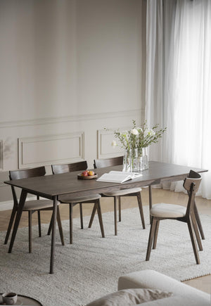 Matbord i mörkt trä med matchande stolar i ljust matrum med vita väggar och gardiner