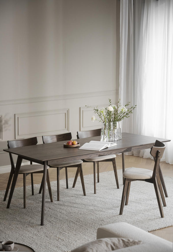 Matbord i mörkt trä med matchande stolar i ljust matrum med vita väggar och gardiner