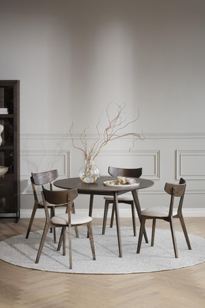 Rund matbord i mörkt trä med fyra stolar och ljus dyna, dekorerat med vas och grenar på rund matta
