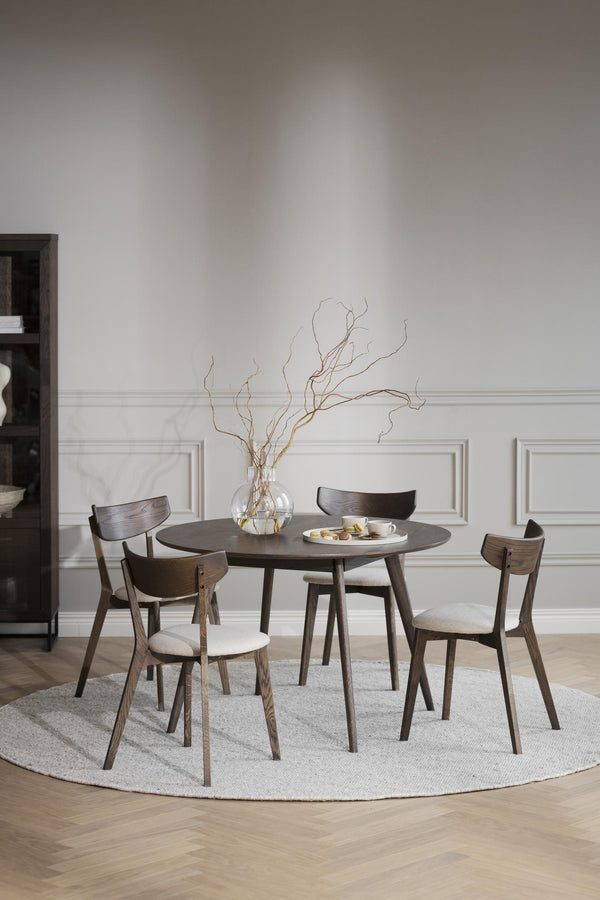 Rund matbord i mörkt trä med fyra stolar och ljus dyna, dekorerat med vas och grenar på rund matta