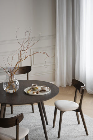 Minimalistiskt matbord i mörk ek med stolar, glasvas med kvistar och kaffeservis i ljust scandinaviskt rum