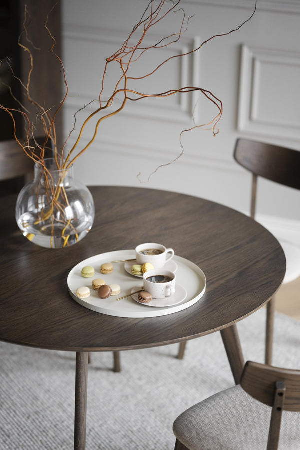 Runt matbord i mörk ek med två stolar, dekorerat med vas och bricka med kaffe och macarons