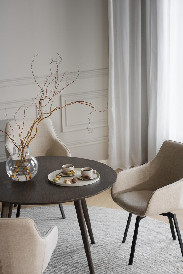 Rund matbord i mörkt trä med beige stolar i modern skandinavisk stil, dekorerat med vas och kaffe