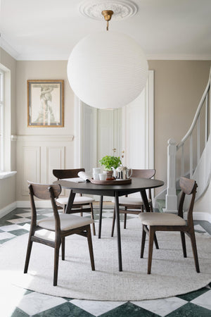 Matgrupp med runt svart bord och fyra stolar i trä med beige klädsel i skandinavisk matsal