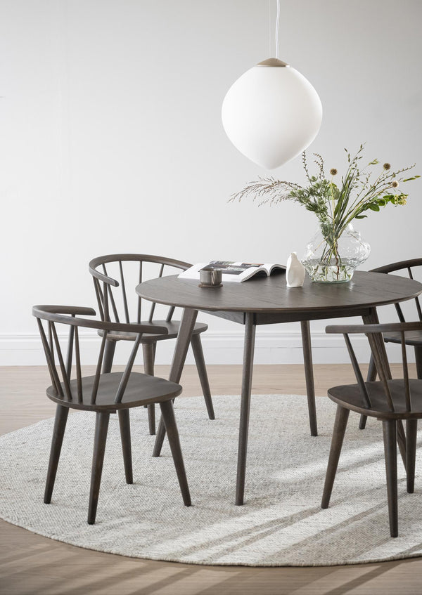 Rund matbord i mörkt trä med matchande pinnstolar i skandinavisk design, lampa och växtdekoration