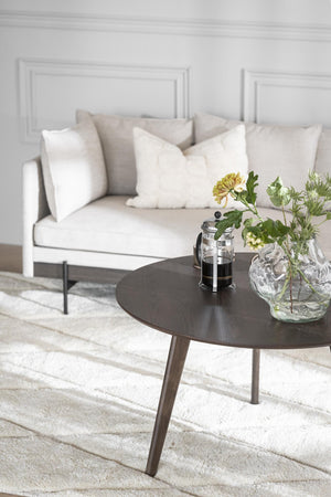 Modernt vardagsrum med vit soffa, beige kuddar, mörkt soffbord och glasvas med blommor på ljus matta