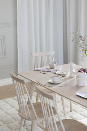 Ljust matbord i trä med matchande pinnstolar, uppdukat med vita porslinskoppar och vas med torkade blommor