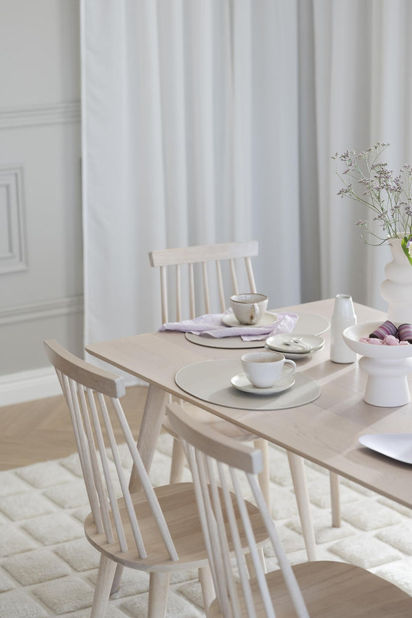 Ljust matbord i trä med matchande pinnstolar, uppdukat med vita porslinskoppar och vas med torkade blommor