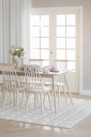 Ljus matplats med ljust trämöblemang, spjälstolar runt matbord på vit matta framför glasdörr