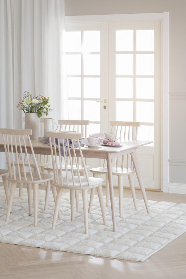 Ljus matplats med ljust trämöblemang, spjälstolar runt matbord på vit matta framför glasdörr