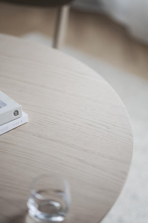 Runt matbord i vit ek med elegant trästruktur och vita metallben, närbild av bordsskiva