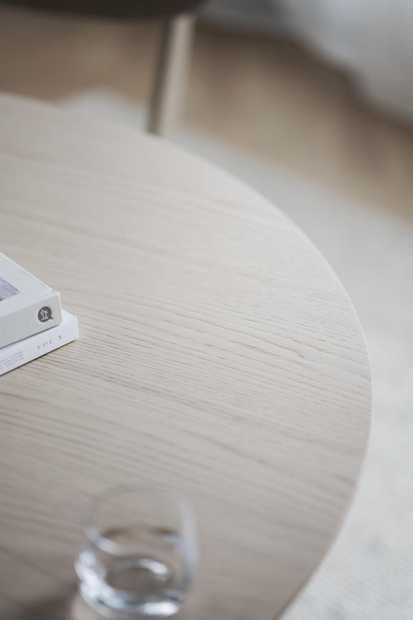 Runt matbord i vit ek med elegant trästruktur och vita metallben, närbild av bordsskiva