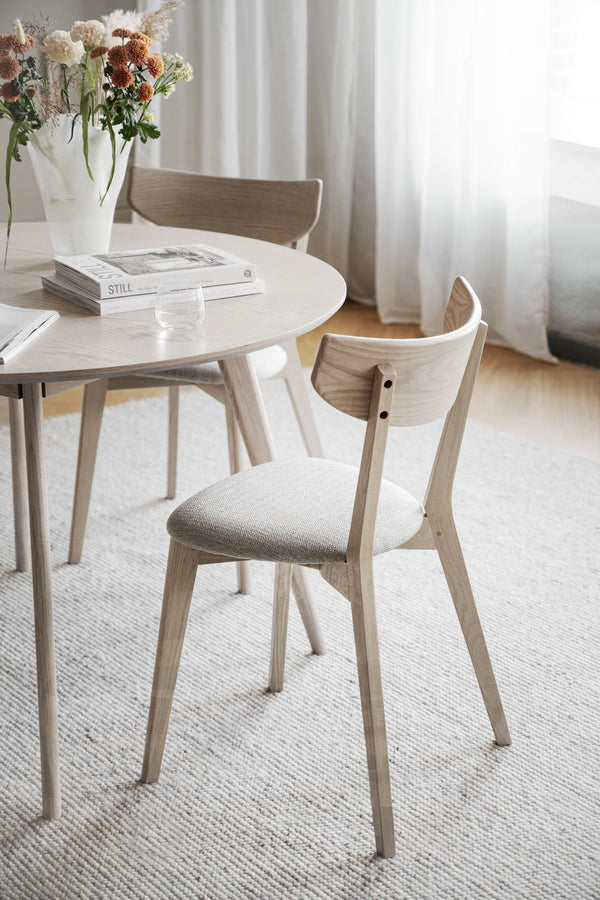 Ljus trämatgrupp med runda bordet och stolar med stoppad sits i naturliga toner på vit matta