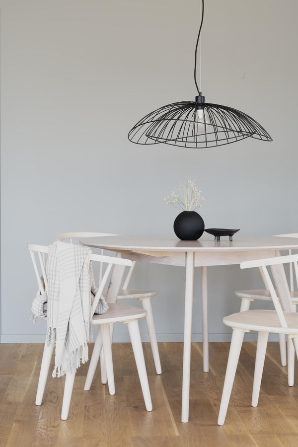 Svart taklampa i wiredesign över runt matbord i ljust trä med vita pinnstolar i skandinavisk stil
