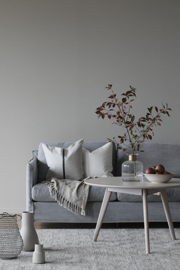 Grå soffa med vita kuddar, pläd och soffbord i skandinavisk stil med vas och dekorationer