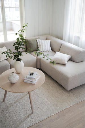 Beige modulsoffa med kuddar i ljust vardagsrum med runt soffbord och växt