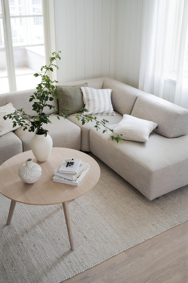 Beige modulsoffa med kuddar i ljust vardagsrum med runt soffbord och växt