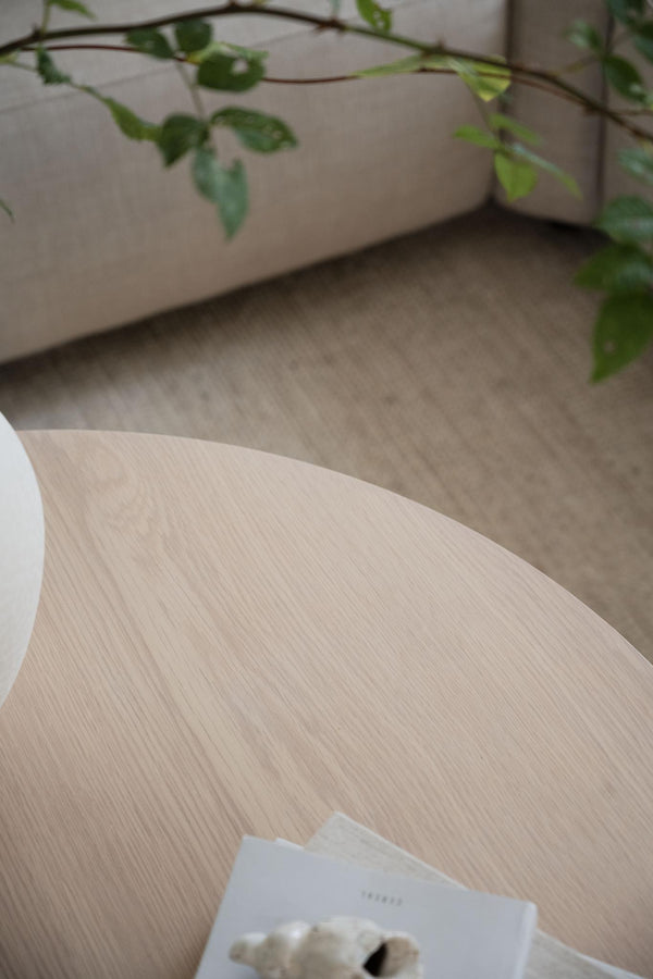 Ljust träbord med synlig åderstruktur och grön växtdekoration i bakgrunden