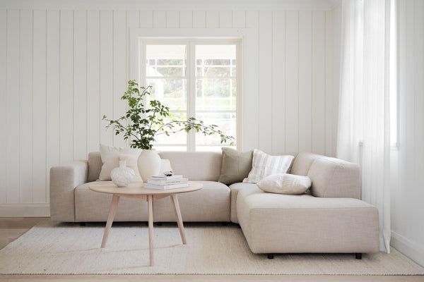 Beige modulsoffa med ljust träbord i skandinaviskt vardagsrum med vita väggar och naturligt ljus