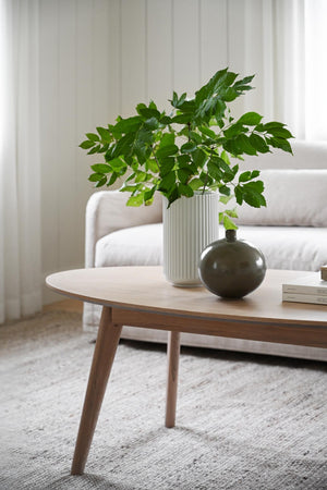 Soffbord i ljust trä med vit räfflad vas med gröna kvistar och grön keramikvas i skandinavisk stil