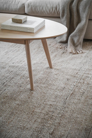 Runt soffbord i ljust trä med böcker på vit luggmatta framför grå soffa med filt