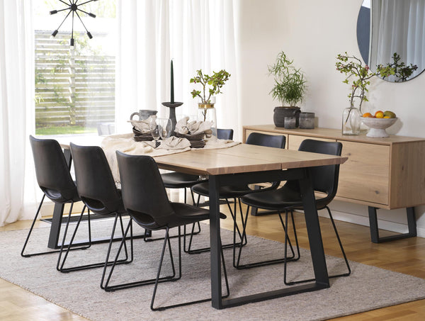 Matgrupp med bord i ljust trä och svarta stolar, matbord med svart metallstativ och matchande skänk