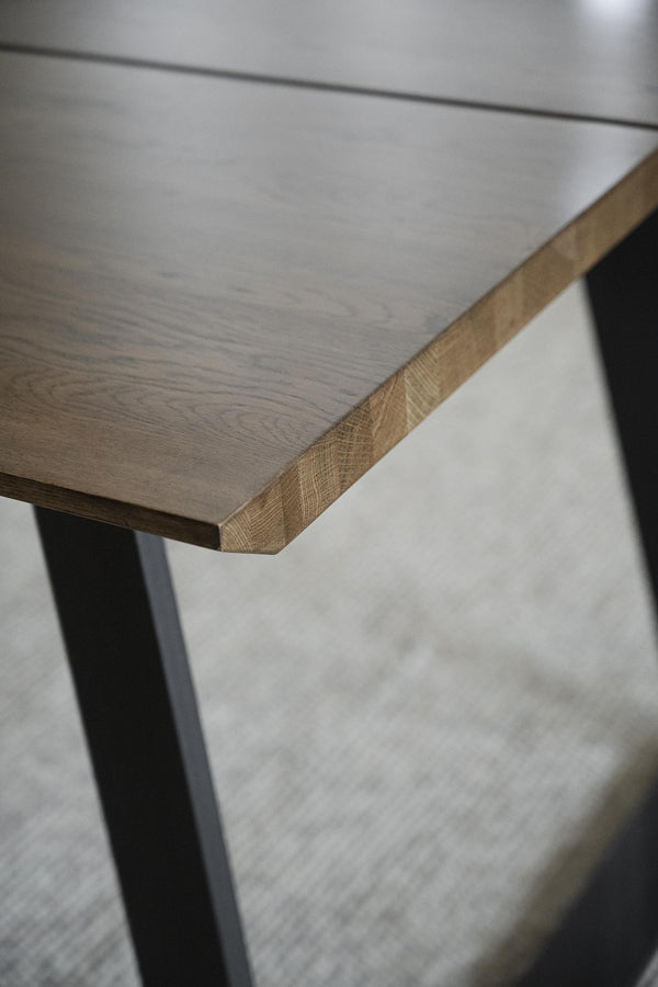 Närbildsdetalj av bordsplatta i ek med svarta metallben, visar trästruktur och hantverk