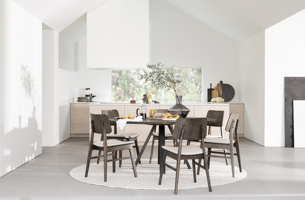 Matgrupp med runt bord och sex stolar i mörkt trä på rund matta i ljust minimalistiskt matrum