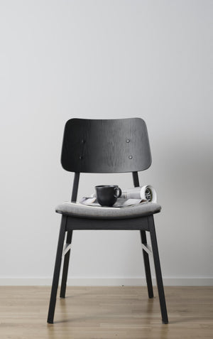 Svart stol i trä med grå dyna, dekorerad med kaffekopp och tidning på sits