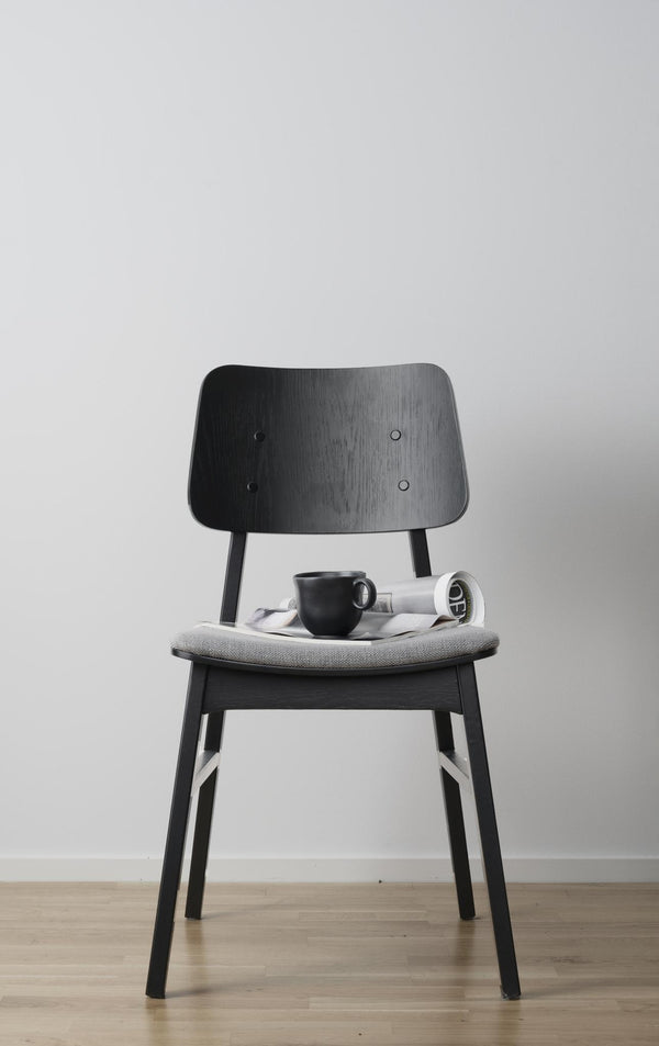 Svart stol i trä med grå dyna, dekorerad med kaffekopp och tidning på sits