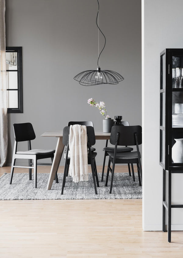 Minimalistisk matplats med svarta stolar, runt matbord och svart wirelampa över grå vägg