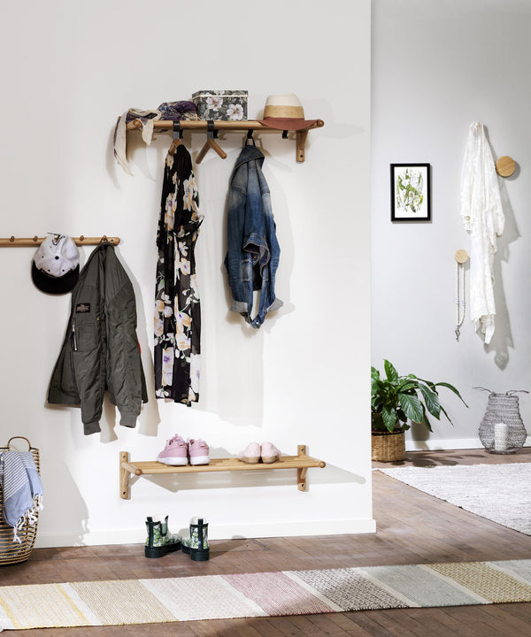 Hallmöbler i trä med klädhängare, hyllplan och krokar monterade på vit vägg med jackor och accessoarer