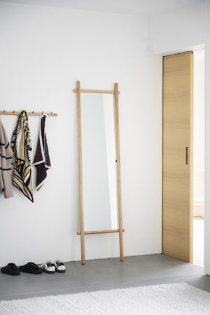 Spegel med ekram i hallmiljö bredvid klädhängare med scarfs och öppen dörr med skor på golvet