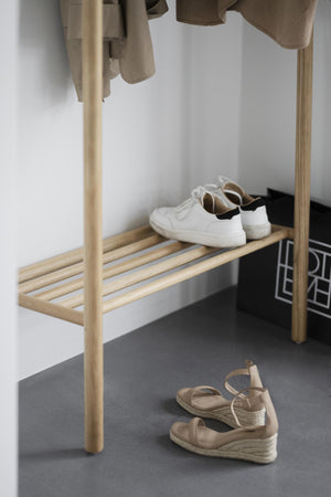 Hallmöbel i ljust trä med kläderhängare och skohylla, vita sneakers och beiga sandaletter