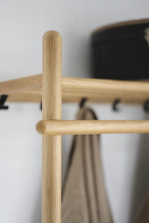 Klädhängare i ljust trä med rundad design och beige kappa i bakgrunden