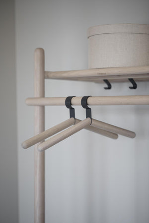 Klädhängare i trä med svarta krokar på klädställning bredvid lampa med linneskärm