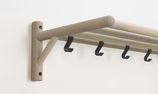 Väggmonterad klädhängare i ljust trä med fyra svarta krokar och snedställt stöd