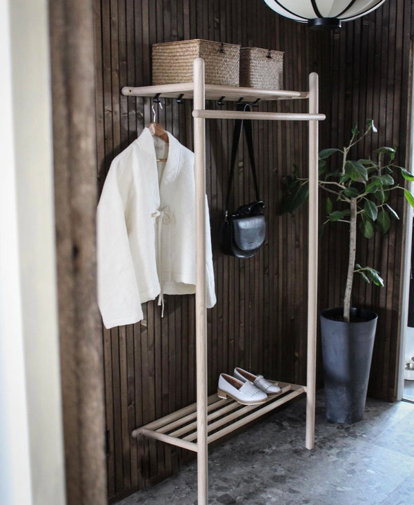 Klädställning i ljust trä med hyllor, krokar och skohylla i modern hallmiljö med växt och korgar