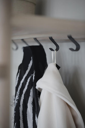 Klädhängare med svarta krokar på väggen med upphängd randig halsduk och vit handduk