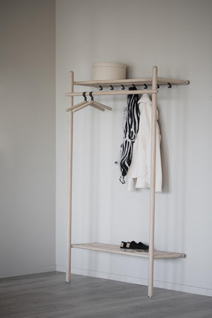 Minimalistisk klädställning i ljust trä med krokar, hylla och garderob mot vit vägg