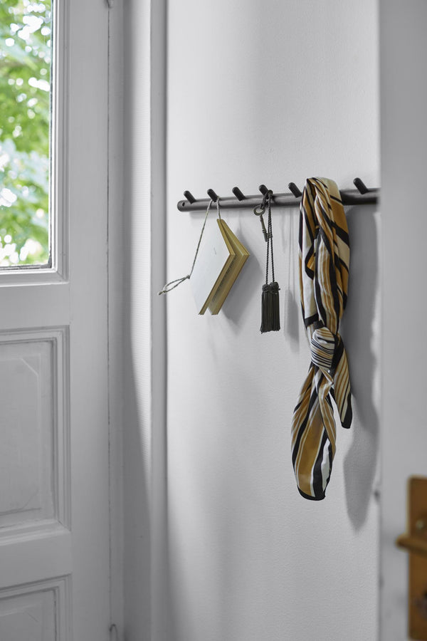 Svart väggkrok med flera krokar med upphängd spegel, tassel och mönstrat paraply i entré