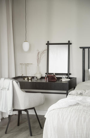 Sovrum med sminkbord i mörkt trä, vit stol, spegel och vit pendellampa i minimalistisk stil