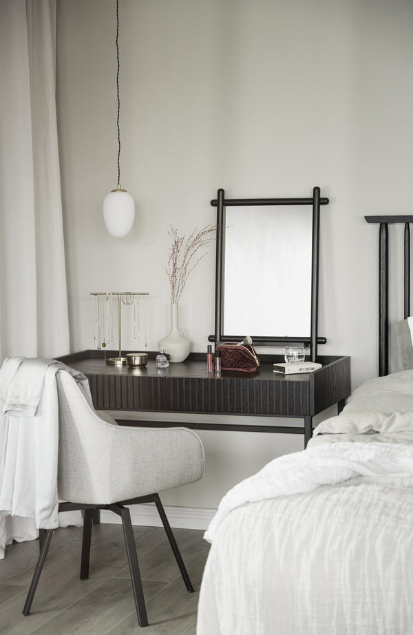 Sovrum med sminkbord i mörkt trä, vit stol, spegel och vit pendellampa i minimalistisk stil