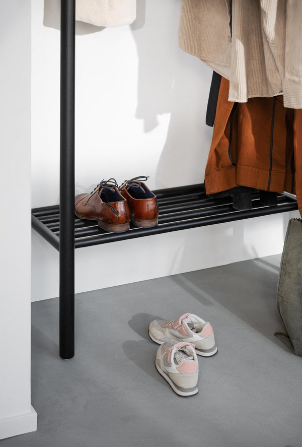 Skoställ i svart metall med bruna läderskor på hylla och vita sneakers på golvet i hall