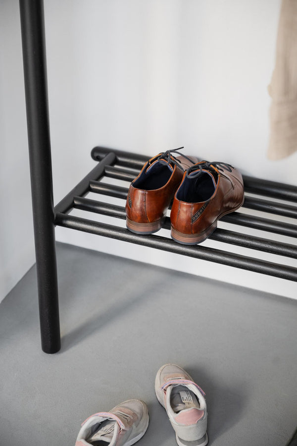 Skoställ i svart metall med bruna läderskor och sneakers på grått golv