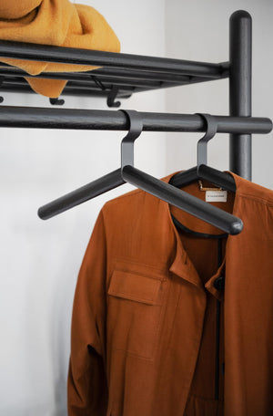 Svart klädhängare i metall med orange jacka och gul mössa på väggmonterad klädställning