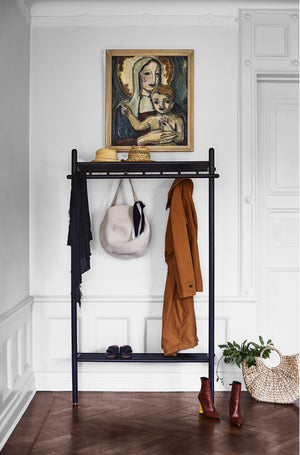 Svart klädhängare med hylla och krokar i hall, med kläder, väska och skor, tavla på väggen