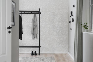 Svart klädställning i metall med hängande kläder i minimalistisk hall med ljusa väggar