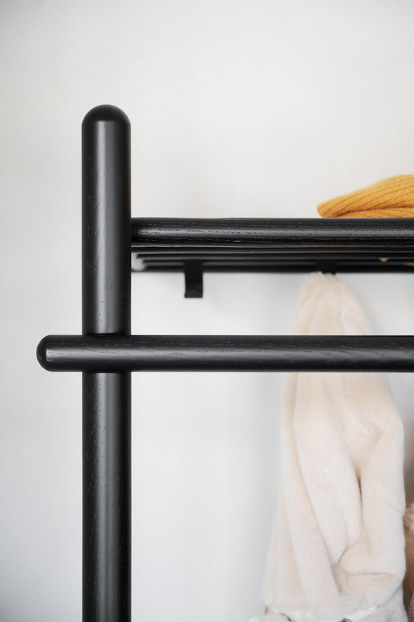 Svart klädhängare i metall med hängande kläder i beige och gult, närbild på modern design