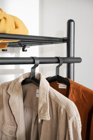 Svart klädhängare i metall med cordjackor i beige och bruna toner på vit vägg